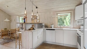 A modern kitchen with white cabinets, a wooden countertop, and a built-in dishwasher. There are hanging light fixtures and a window providing natural light.