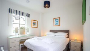 Un dormitorio ordenado con cama, mesitas de noche, un escritorio y una ventana con cortinas.