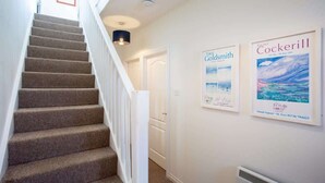 Una escalera con escalones alfombrados y barandillas blancas que conduce a una puerta. Dos carteles enmarcados decoran la pared.