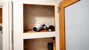 A shelf with a hairdryer and a black device, possibly a hair straightener, against a floral wallpaper background. - Vintage RV & SPA Experience for 3 (Dover)