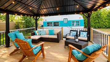 A covered outdoor deck with wooden furniture and a blue RV in the background.