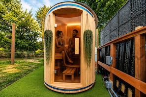 A wooden sauna with two benches, surrounded by greenery and a black mesh wall. - Vintage RV & SPA Experience for 3 (Dover)