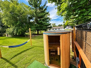 A wooden playhouse with a door, a hammock, and a fenced area with trees and a house in the background. - Vintage Rv & Spa Experience for 3 (Dover)