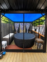 A circular outdoor seating area with a round table and benches, surrounded by a wooden deck and a blue canopy.