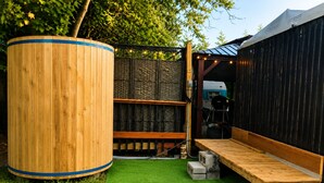 A wooden outdoor seating area with a green artificial turf, a large cylindrical object, and a black structure with a sloped roof. - Vintage Rv & Spa Experience for 3 (Dover)