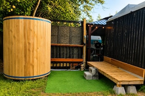 A wooden outdoor seating area with a green artificial turf, a large cylindrical object, and a black structure with a sloped roof. - Vintage Rv & Spa Experience for 3 (Dover)