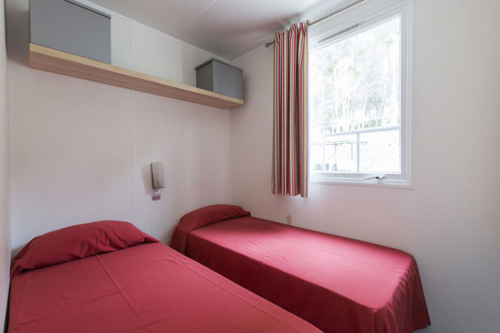Una habitación tipo dormitorio con dos camas individuales, una ventana con cortinas y un estante sobre las camas.
