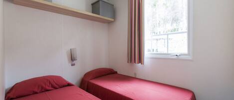 Una habitación tipo dormitorio con dos camas individuales, una ventana con cortinas y un estante sobre las camas.
