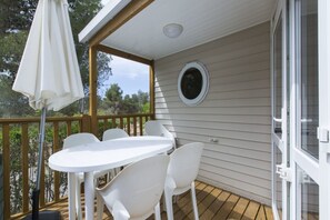 Ein überdachter Außenbereich mit weißem Tisch und Stühlen, einem weißen Sonnenschirm und einer Holzterrasse.