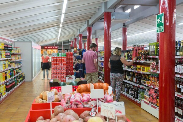 A supermarket aisle with various products on shelves and a display of fresh produce at the end. - Amazing bungalow with parking (la Geltrú, Barcelona)