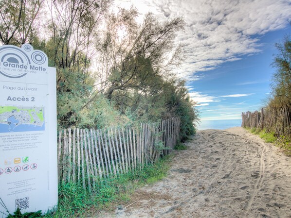 A beach path with a wooden fence, a sign for Grande Motte, and a clear sky.