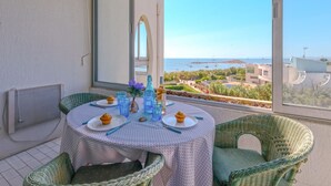 Un balcón con una mesa dispuesta para dos personas, con vistas a la costa, edificios y un puerto deportivo.