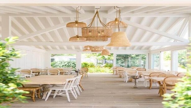 Un espacio interior amplio con techos altos y luz natural, que incluye varias mesas de comedor y sillas de mimbre.