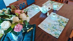A dining table set with floral placemats, a teapot, cups, and a vase with flowers.