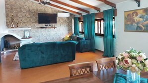 A cozy living room with a stone fireplace, a large TV, and a dining area with wooden furniture.