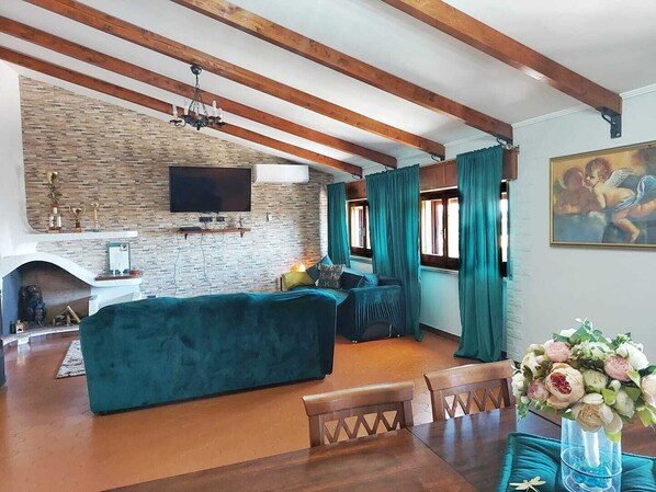 A cozy living room with a stone fireplace, a large TV, and a dining area with wooden furniture.