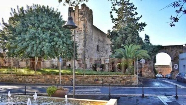 A historic stone building with a bell tower, surrounded by a fence and trees.