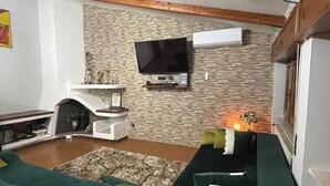 A living room with a stone wall, a mounted TV, a fireplace, and green sofas.