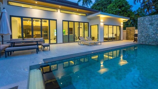 Ein modernes Haus mit Swimmingpool, großen Glasfenstern und einer Steinsäule.
