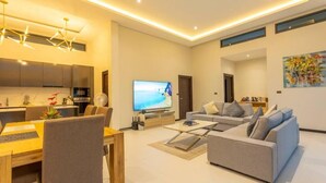 Ein modernes Wohnzimmer mit grauem Sofa, einem Esstisch mit Stühlen, einem Flachbildfernseher und einer Küchenzeile mit Schränken und einer Mikrowelle.