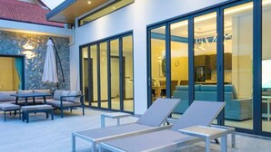 Ein moderner Außenbereich mit Lounge-Möbeln und einem Tisch, einer Steinmauer und einer Glastür, die in ein Wohnzimmer führt.
