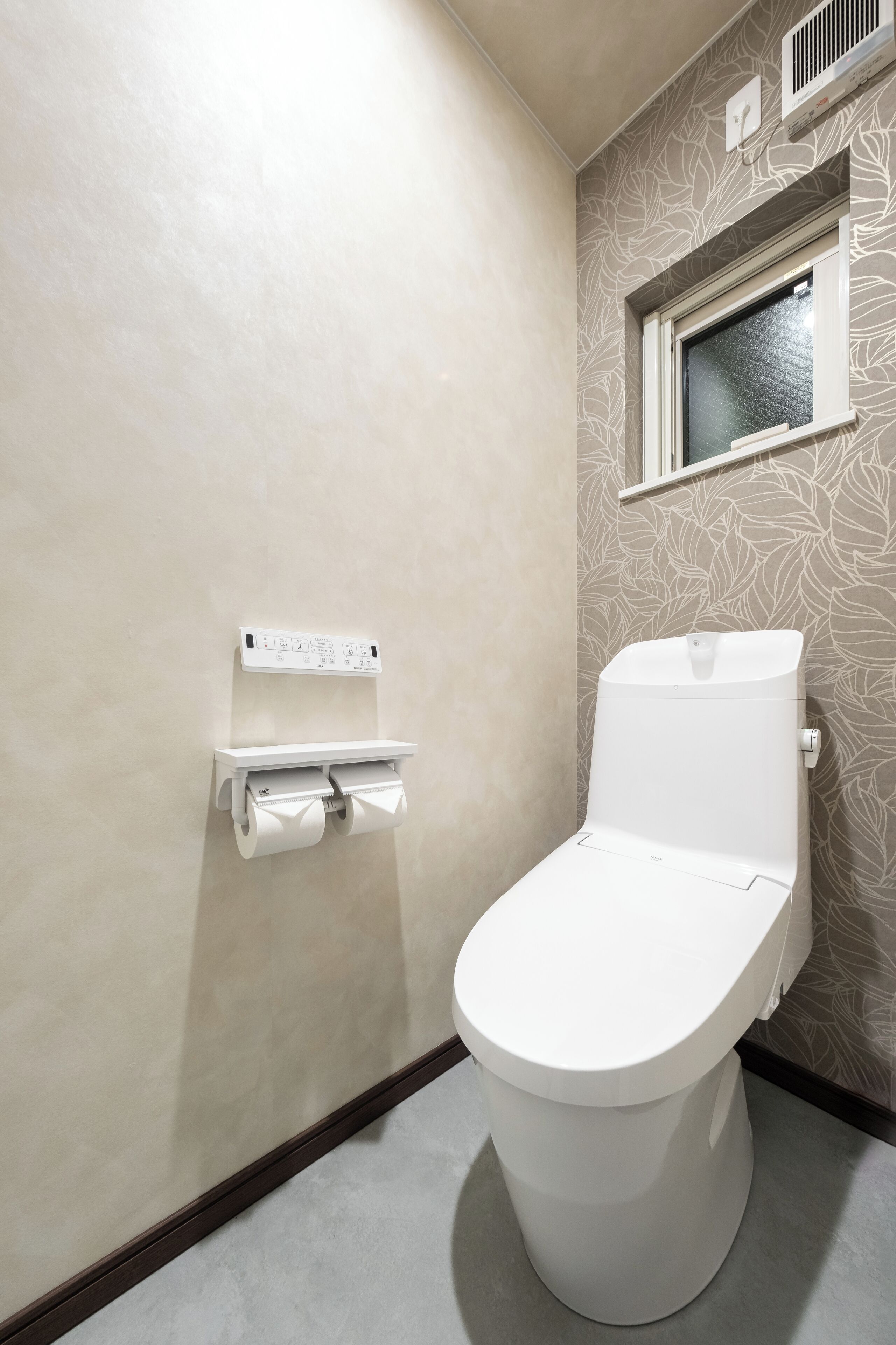 A toilet with a white flush tank and a paper towel dispenser mounted on the wall.