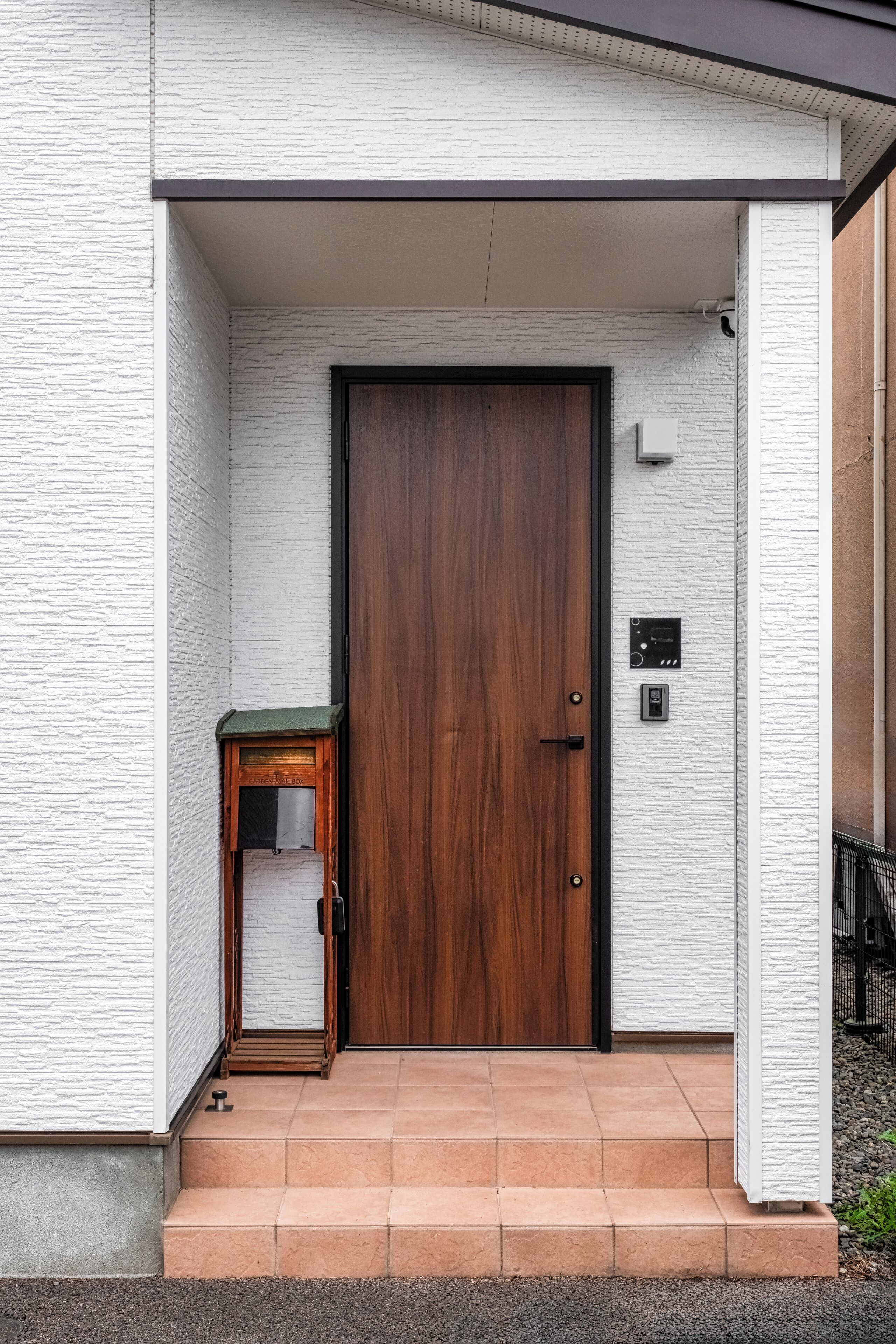 A modern building entrance with a wooden door, a small table, and a wall-mounted intercom.