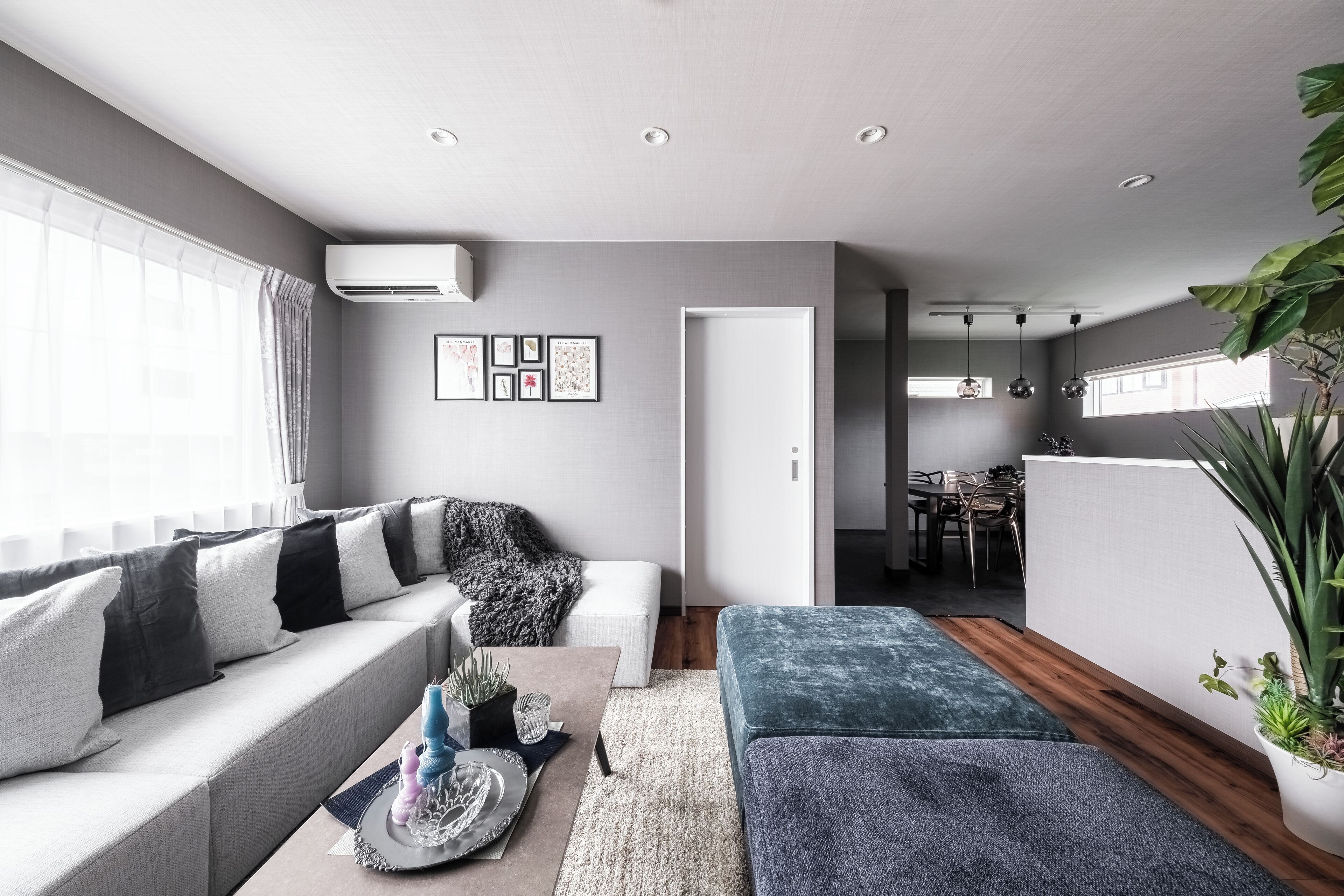 Un salon moderne avec un canapé gris, un pouf bleu et un coin repas à l’arrière-plan.