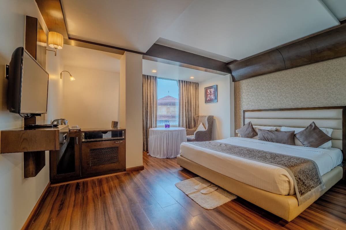 Une chambre d’hôtel avec un grand lit, un bureau avec une télévision, une chaise, une petite table et une fenêtre avec des rideaux.