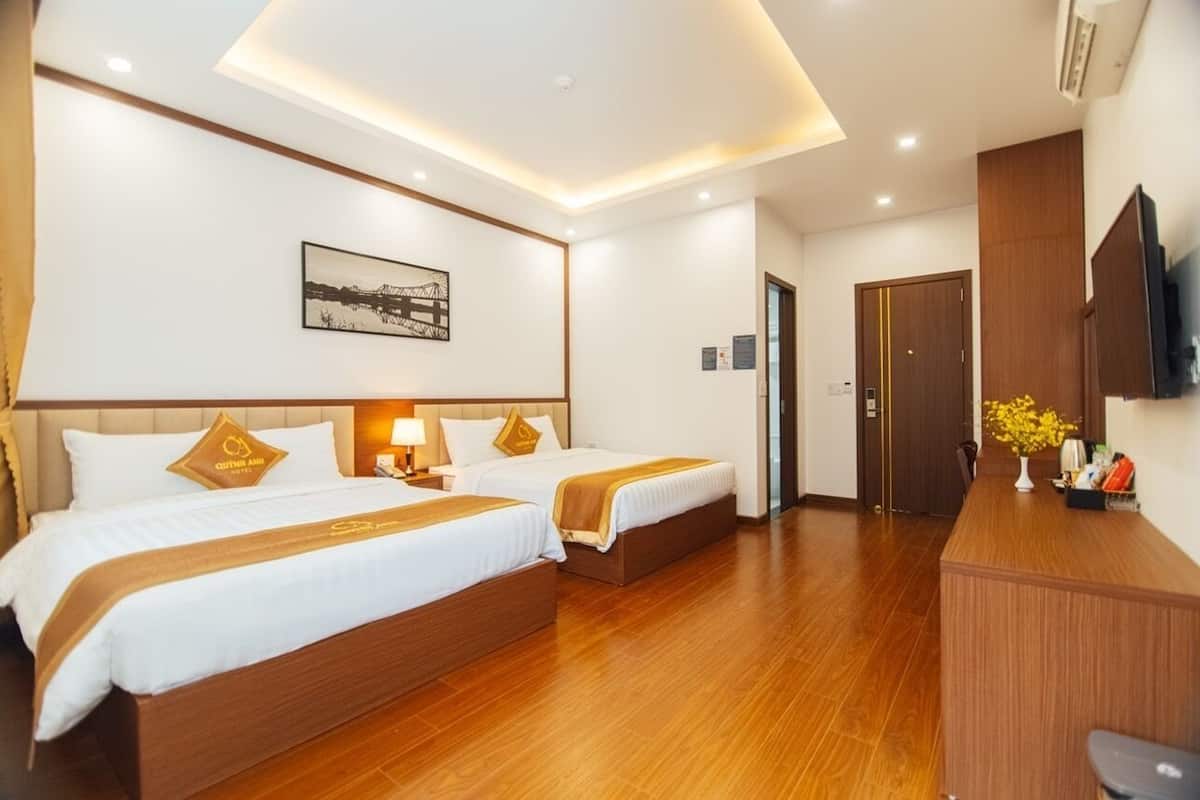 A hotel room with two beds, a desk, a TV, and a framed picture on the wall.