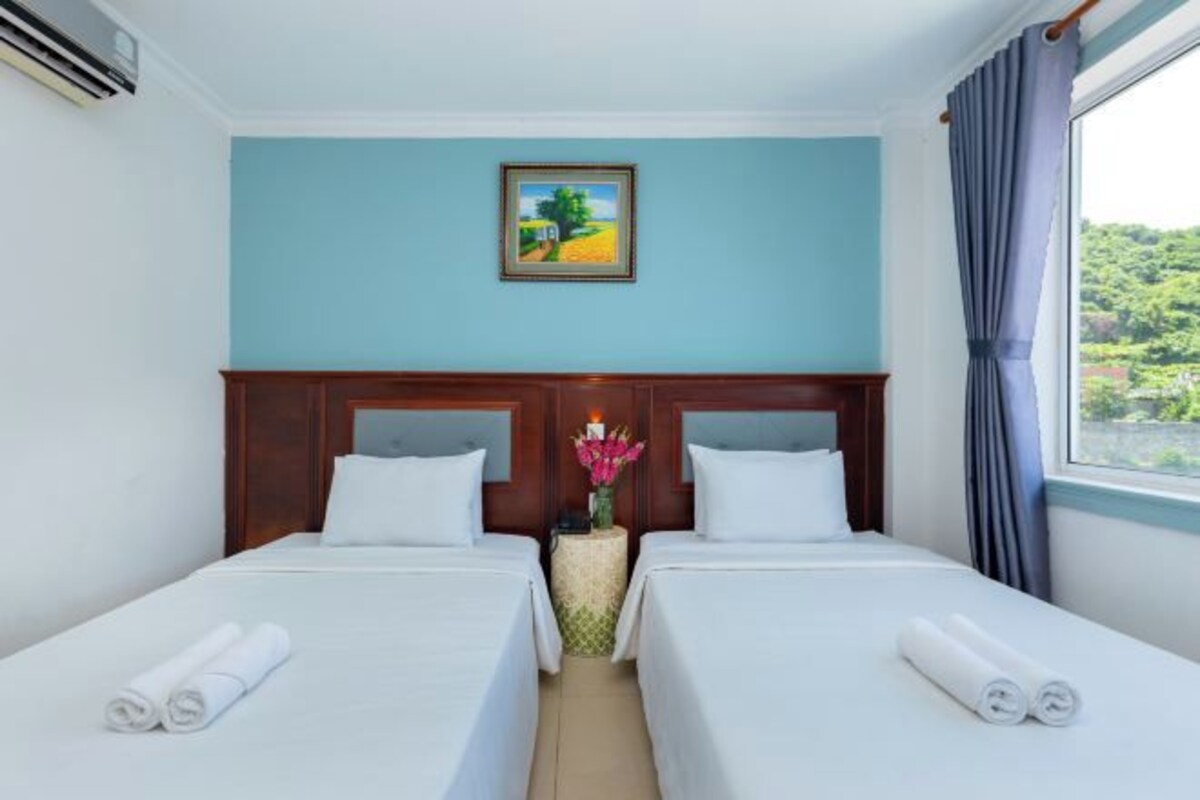 A hotel room with two beds, a painting on the wall, and a window with curtains.