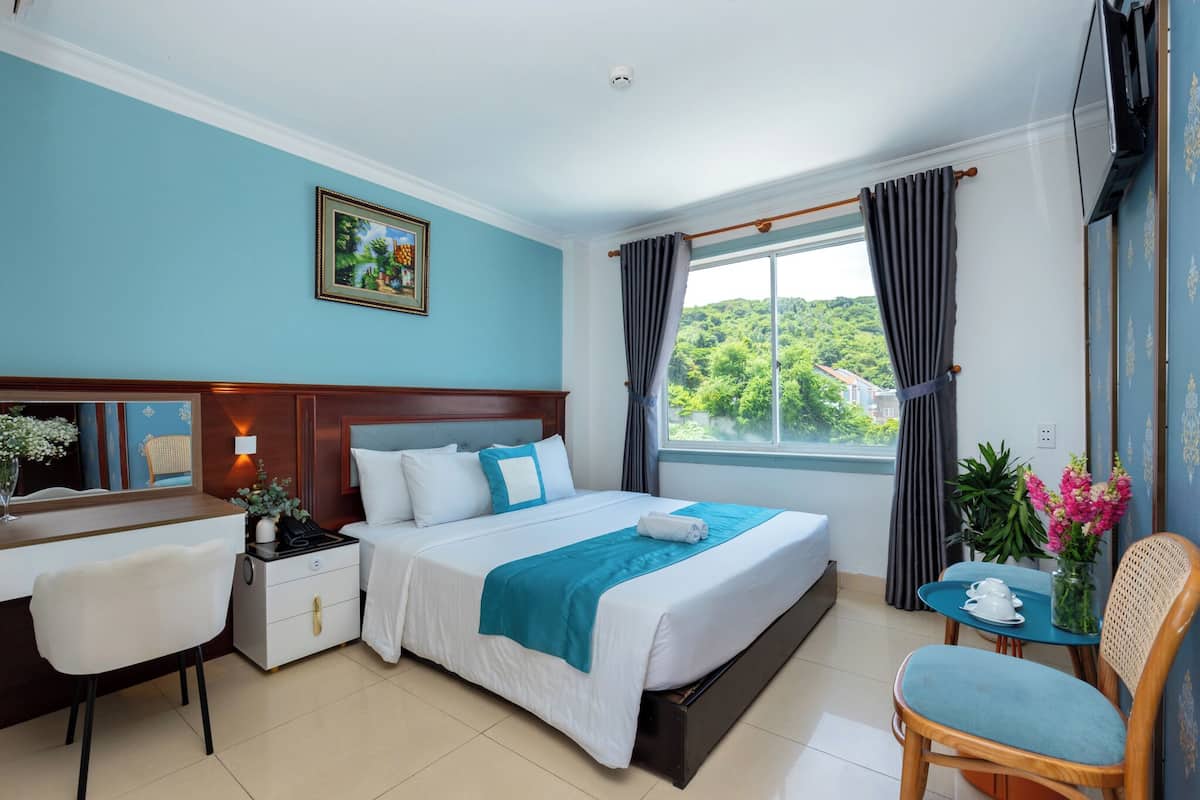 A hotel room with a bed, bedside table, chair, desk, and a window with curtains.