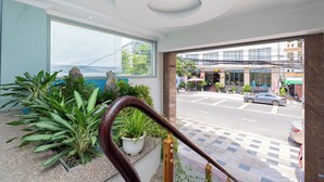 A hotel lobby with a staircase, potted plants, and a view of the street outside.