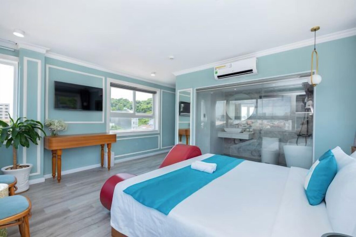 A modern hotel room with a large bed, a desk, and a view of the city.
