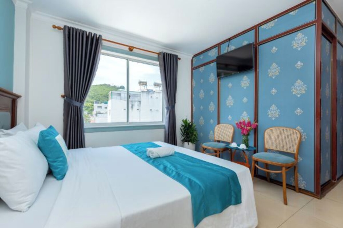 A hotel room with a bed, two chairs, a wardrobe, and a window with curtains.