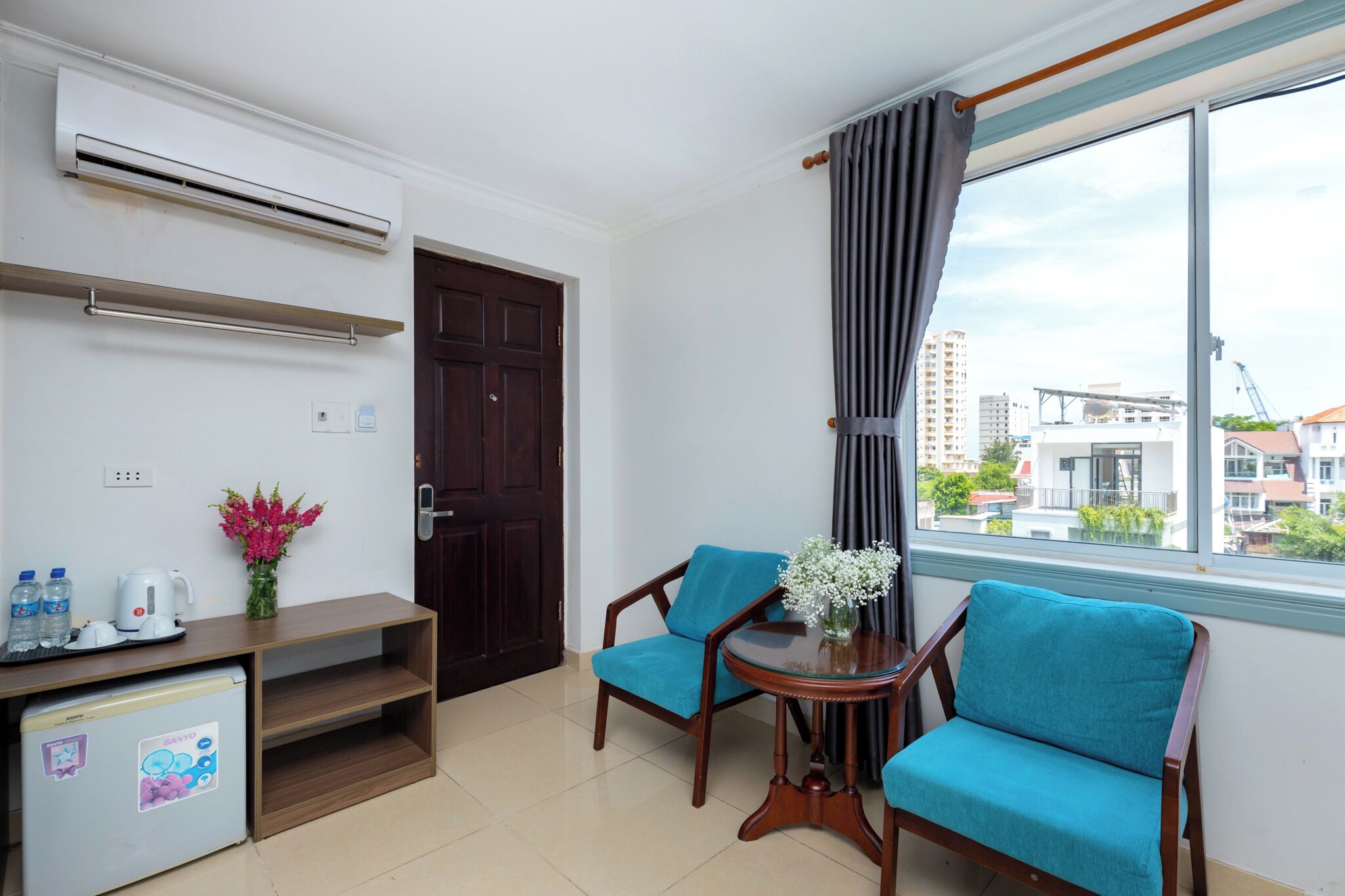 A compact room with a kitchenette, two chairs, a small table, and a window with curtains.