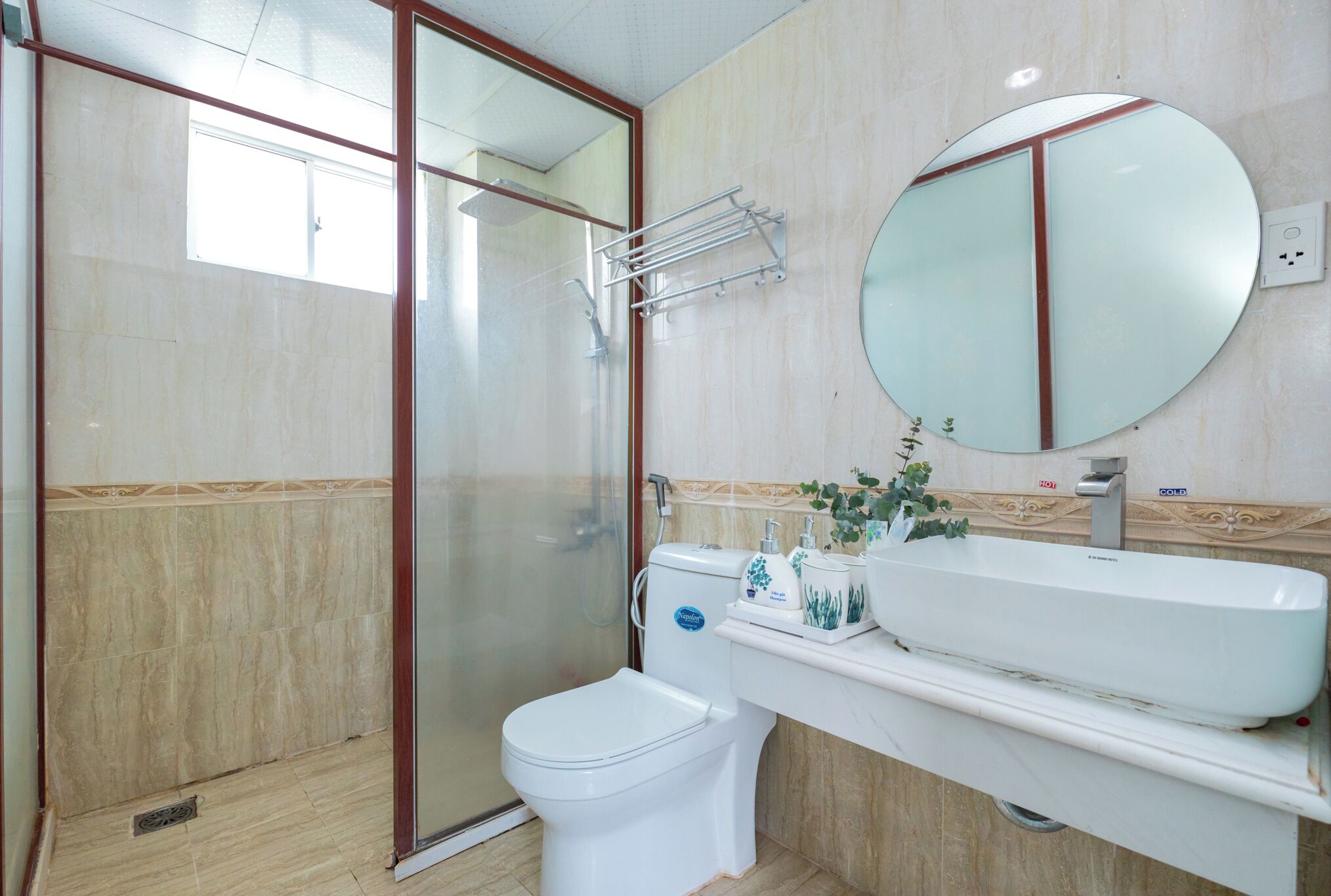 Een badkamer met een douche met glazen wand, toilet, wastafel met spiegel en een plank met toiletartikelen.