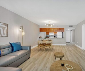 Uma sala de estar moderna com um sofá, uma mesa de jantar e uma cozinha com armários de madeira e eletrodomésticos.