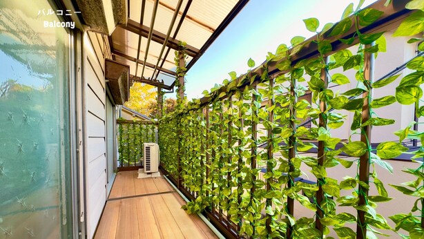 Een balkon met een houten vloer en een metalen trekwerk begroeid met groene bladeren.