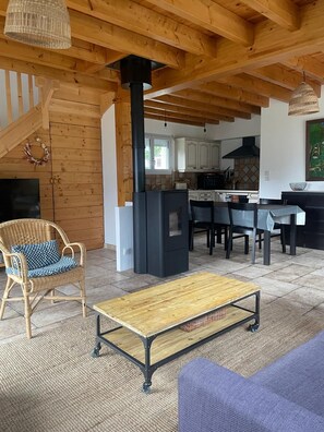 A cozy living area with a fireplace, wooden furniture, and a kitchen in the background.