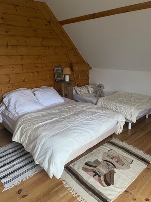 A bedroom with two beds, wooden walls, a small bedside table with a lamp, and a rug.