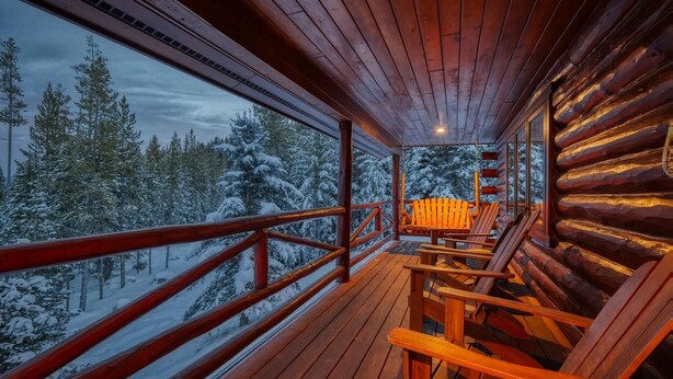 Een houten chalet met een terras, houten stoelen en uitzicht op met sneeuw bedekte bomen.