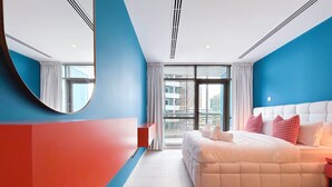 A modern bedroom with a large bed, a round mirror, and a view of the city through the window. - Colorful Studio With Balcony & City Views (Dubai)