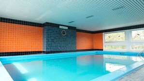 Une piscine intérieure avec un mur carrelé, une horloge et une fenêtre donnant sur des arbres.