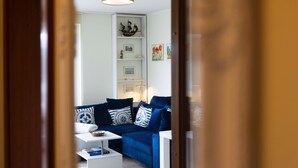 Un salon avec un canapé bleu, une table d’appoint blanche et une bibliothèque agrémentée d’objets décoratifs.