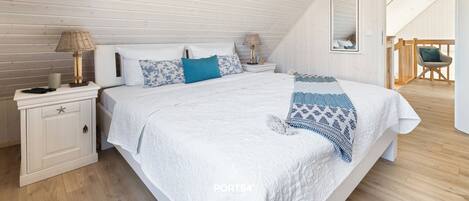 A bedroom with a sloped ceiling, a bed with white bedding, two bedside tables with lamps, a mirror, and a chair.