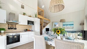 Una cocina moderna con armarios blancos, un horno Bosch y una zona de comedor con sillas de mimbre y una mesa preparada para dos.