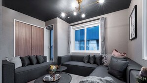 A modern living room with a sectional sofa, a round coffee table with decorative items, a fur rug, and a large window with blue curtains. - THE OBSIDIAN  (Sapporo)