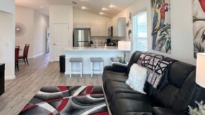 A modern living room with a black leather sofa, a patterned rug, and a ceiling fan. - Dessert First - Cozy 2/2 in The Village of DeLuna Accepts a Small Dog with pre-approval (The Villages)