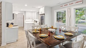 Una cocina moderna con armarios blancos, una mesa de madera con capacidad para seis comensales y un letrero sobre la mesa que enumera productos del mar.